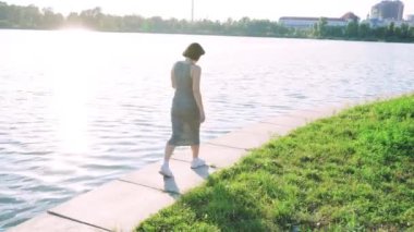 Nehir kenarında sakin bir yürüyüş yapan bir kadın. Arka planda yeşillik ve su var. Açık hava, yaşam tarzı ve rahatlama temaları için mükemmel.