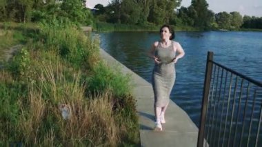 Gün batımında sakin bir nehrin kenarında yürüyen bir kadın huzurlu ve huzurlu bir atmosfer yaratıyor. Rahatlama, doğa ve açık hava yaşam tarzı görüntüleri için harika.