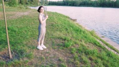 Gün batımının yumuşak ışığında doğa tarafından çevrelenmiş bir kadın nehri boyunca yürüyor. Doğa ve açık hava yaşam tarzı içeriği için ideal