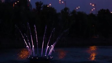 Göz kamaştırıcı gece çeşmesi görüntüsü. Parlak renkli su püskürtüleri. LED ışıklarıyla aydınlatılıyor, karanlıkta zarif bir şekilde dans ediyor.