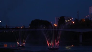 Göz kamaştırıcı gece çeşmesi görüntüsü. Parlak renkli su püskürtüleri. LED ışıklarıyla aydınlatılıyor, karanlıkta zarif bir şekilde dans ediyor.