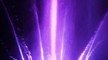 Göz kamaştırıcı gece çeşmesi görüntüsü. Parlak renkli su püskürtüleri. LED ışıklarıyla aydınlatılıyor, karanlıkta zarif bir şekilde dans ediyor.