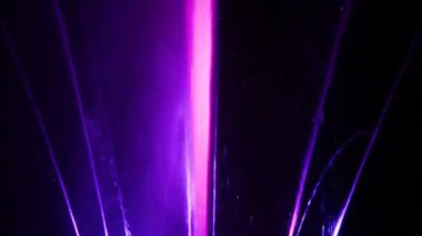 Karanlık arka plan. Büyük renkli dekoratif dans jeti geceleri hafif fıskiye gösterisine öncülük etti. Güzel bir lazer ve fıskiye gösterisi. Renkli su çeşmeleri