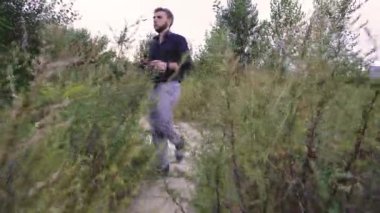 Genç bir adam koyu yeşil bir tişörtle sık ve yeşil bir arazide geziniyor. Doğadaki sakin ve huzurlu bir anı yakalamak, yalnızlık, farkındalık ve açık hava yaşam tarzı kavramları için idealdir.