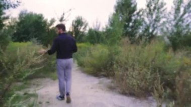 Yeşilliklerle çevrili kentsel alanda rahatça gezinen genç bir adamın arka görüntüsü. Yaşam tarzı ve açık hava sahneleri için uygun