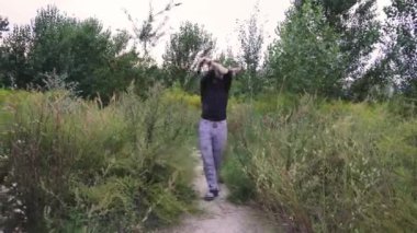 Genç bir adam koyu yeşil bir tişörtle sık ve yeşil bir arazide geziniyor. Doğadaki sakin ve huzurlu bir anı yakalamak, yalnızlık, farkındalık ve açık hava yaşam tarzı kavramları için idealdir.