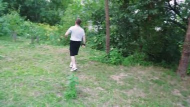 Koyu renk tişörtlü bir adam yemyeşil, fazla gelişmiş bir bölgeyi keşfediyor. Yeşillikte yavaşça yürüyor, doğada sakin bir sahne yaratıyor. Macera, rahatlama ve yalnızlık temaları için mükemmel.