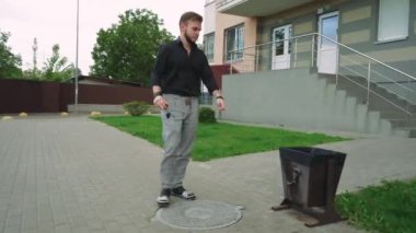 Siyah tişörtlü ve gri kotlu vahşi bir adam kaldırım boyunca yürür konut binalarının arka planında