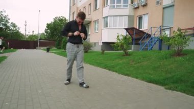 Güneş gözlüklü bir adam yeşil bir parkta bir şehir tarafından çevrili bir fayans yolu boyunca yürür. Rahatlama, yalnızlık ve açık hava yaşam tarzı temaları için mükemmel.