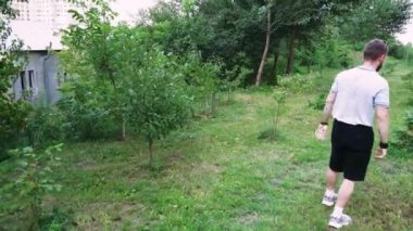 Etrafı yeşilliklerle çevrili, sakin bir park ortamında yürüyen bir adam. Yaşam tarzı ve doğa odaklı videolar için harika.