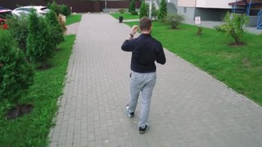 Siyah tişörtlü ve gri kotlu vahşi bir adam kaldırım boyunca yürür konut binalarının arka planında