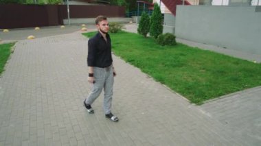 Koyu renk gömlekli bir adam şehirde ve yabani bitki örtüsünde yürüyor. Sessiz bir an macera, doğal güzellik ve farkındalık temalarını vurgular.