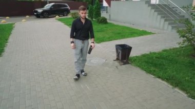 Elinde bir fincan çay olan bir adam konut binalarının yakınındaki yeşil bir parkta yürüyor. Rahatlama, yalnızlık ve açık hava yaşam tarzı temaları için mükemmel.