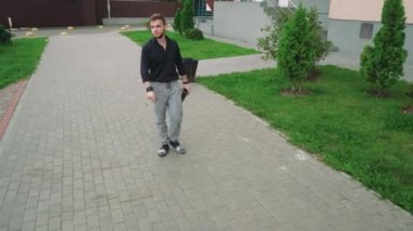 Siyah tişörtlü ve gri kotlu vahşi bir adam kaldırım boyunca yürür konut binalarının arka planında