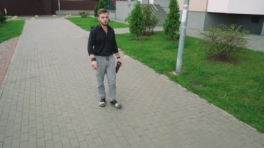 Elinde bir fincan çay olan bir adam konut binalarının yakınındaki yeşil bir parkta yürüyor. Rahatlama, yalnızlık ve açık hava yaşam tarzı temaları için mükemmel.