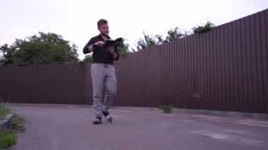 Bir adam, elinde bir kitapla, kahverengi metal bir çitin arkasında huzurlu bir şekilde yürümekten hoşlanır. Bu huzurlu sahne görsel rahatlama, huzur ve doğa keşfi içindir.