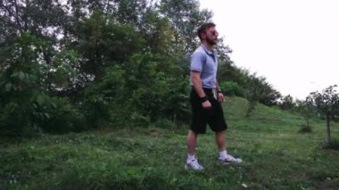 Genç adam yemyeşil bir park alanında yürüyor, yemyeşil bitkiler ve ağaçlarla çevrili. Yaşam tarzı ve açık hava rahatlama temaları için mükemmel