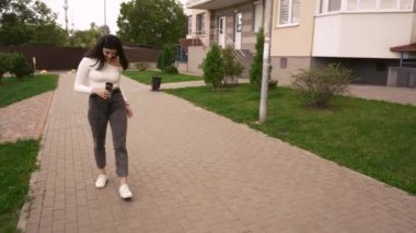 Sıradan giyinmiş, ceketli bir kadın yeşil kentsel alanda yürüyor. Etrafı apartmanlarla çevrili. Modern yaşam tarzı ve kentsel imajlar için uygun