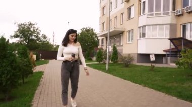 Sıradan giyinmiş, ceketli bir kadın yeşil kentsel alanda yürüyor. Etrafı apartmanlarla çevrili. Modern yaşam tarzı ve kentsel imajlar için uygun