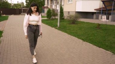 Yaşam tarzı ve şehir temaları için mükemmel bir sahne. Genç bir kadın pembe ceketli, modern bir apartmanın yanında rahatça yürüyor..