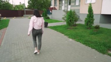 Genç bir kadın, pembe ceketli, modern bir apartmanın yanında güvenle yürüyor. Yaşam tarzı ve kentsel yaşam temaları için mükemmel bir sahne