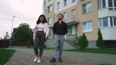 Bir erkek ve bir kız yeşil bir zemine sahip bir apartmanın yakınında güvenle yürüyorlar. Kentsel yaşam tarzı ve moda içeriği için ideal