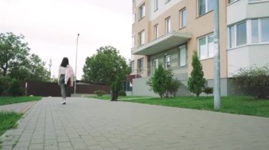 Kendine güvenen genç bir kadın, şehir hayatıyla modayı birleştiren bir apartmanın yakınında bir patika boyunca koşuyor. Yaşam tarzı ve yerleşim görselleri için harika