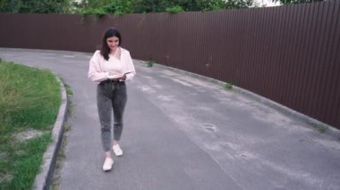 Yaşam tarzı ya da eğlence videoları için ideal. Sessiz bir yolda yürüyen genç bir kadın kitap okuyor ve doğada huzurlu bir anın tadını çıkarıyor.