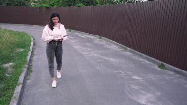 Yaşam tarzı ya da eğlence videoları için ideal. Sessiz bir yolda yürüyen genç bir kadın kitap okuyor ve doğada huzurlu bir anın tadını çıkarıyor.