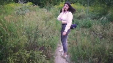 Doğal ortam onun dinlenmesine huzurlu bir an ekliyor. Bir kız yeşil bir yolda yürüyor, akıllı telefonuna bakıyor.