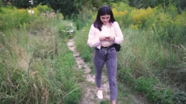 Doğal ortam onun dinlenmesine huzurlu bir an ekliyor. Bir kız yeşil bir yolda yürüyor, akıllı telefonuna bakıyor.