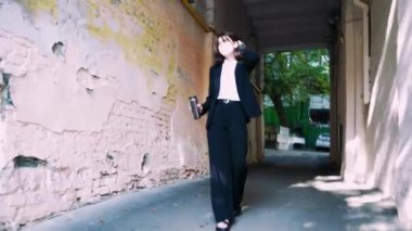 Bir kemer yolunda emin adımlarla ilerleyen, siyah takım elbiseli bir kadın, modern karmaşıklığı aktaran ve tamir edilmesi ve yer değiştirmesi gereken bir evin cephesi tarafından çerçevelenir.