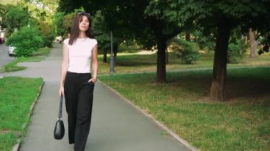 Kafasında gözlük olan siyah saçlı bir kız parkta günün tadını çıkarıyor. Kız parkın arka sokağında yürüyor ve elinde siyah bir çanta taşıyor.
