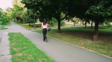 Kafasında gözlük olan siyah saçlı bir kız parkta günün tadını çıkarıyor. Kız parkın arka sokağında yürüyor ve elinde siyah bir çanta taşıyor.
