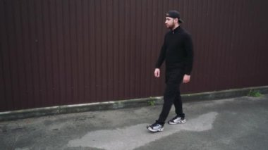 Simsiyah giyinmiş, güneş gözlüklü ve beyzbol şapkalı şık bir adam şehir sokaklarında yürüyor. Basit ama modern moda.