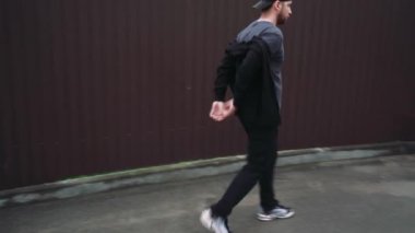 Simsiyah giyinmiş, güneş gözlüklü ve beyzbol şapkalı şık bir adam şehir sokaklarında yürüyor. Basit ama modern moda.