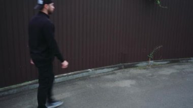 Simsiyah giyinmiş, güneş gözlüklü ve beyzbol şapkalı şık bir adam şehir sokaklarında yürüyor. Basit ama modern moda.