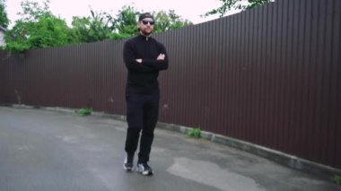 Güneş gözlüğü takan şık bir adam ve günlük siyah kıyafetler bulutlu bir günde şehir caddesinde yürüyor.