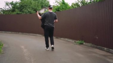 Siyah giysili genç bir adam kaldırımlı bir cadde boyunca güneş gözlüğü ve beyzbol şapkası takarak güvenle yürüyor. Kentsel sokak tarzı