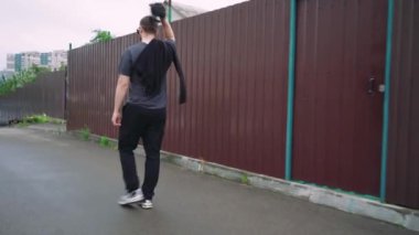 Siyah giysili genç bir adam kaldırımlı bir cadde boyunca güneş gözlüğü ve beyzbol şapkası takarak güvenle yürüyor. Kentsel sokak tarzı