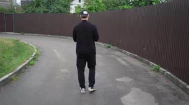 Siyahlı bir adam elinde kitapla şehir caddesinde yürüyor. Önünde kahverengi metal bir çit ve modern binalar var. Kentsel yaşam tarzı, modern yaşam ve gelişigüzel anlar için mükemmel