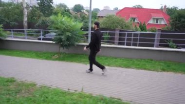 Günlük giysiler giymiş bir adam arka planda yeşillikle şehir caddesinde yürüyor. Kentsel yaşamı, modern yaşamı ve günlük aktiviteleri gösteren videolar için uygundur