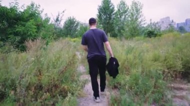 Siyah eşofmanlı bir adam vahşi bitkiler ve ağaçlarla çevrili doğa yürüyüşü patikalarını keşfediyor. Doğa, macera ve açık hava videoları için uygun