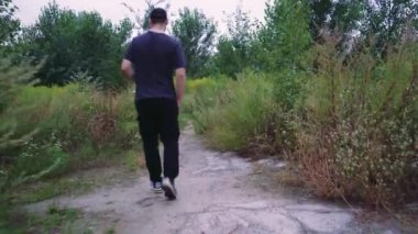 Siyahlı bir adam uzun otlar ve ağaçlarla çevrili toprak bir patikada yürüyor, dışarıda sakin bir anın tadını çıkarıyor. Yürüyüş, doğa ya da yalnızlık temaları için harika.