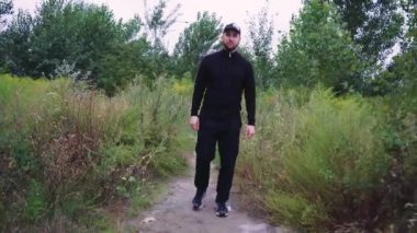 Vahşi bitki örtüsüyle çevrili doğa yolunda seyahat eden bir insan. Adam siyah eşofman ve şapka giyiyor. Doğa yürüyüşleri, yürüyüş ya da sessiz doğa için idealdir.