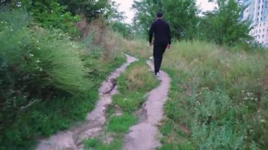 Yalnız bir adam yeşilliklerle çevrili kırsalda yeşil bir yol boyunca yürüyor. Yürüyüş, eğlence ya da macera için ideal
