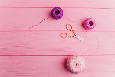 A roll of pink and purple skeins of thread and iron scissors lie on a wooden pink surface, perfect for decorating, gift wrapping and sewing clipart