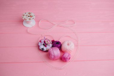 Dökülmüş dantel kalpte örgü örmek için iplik izleri var. Açılış kurdelesi ve iplik elementleri pembe arka planda uyumlu bir şekilde birleştirilir.