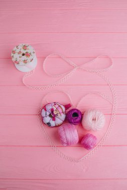 Dökülmüş dantel kalpte örgü örmek için iplik izleri var. Açılış kurdelesi ve iplik elementleri pembe arka planda uyumlu bir şekilde birleştirilir.