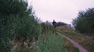 Çevresi yemyeşil bitki örtüsüyle çevrili doğa yolunda yürüyen bir adam. Açık hava, doğa keşfi veya seyahatle ilgili videolar için mükemmel.